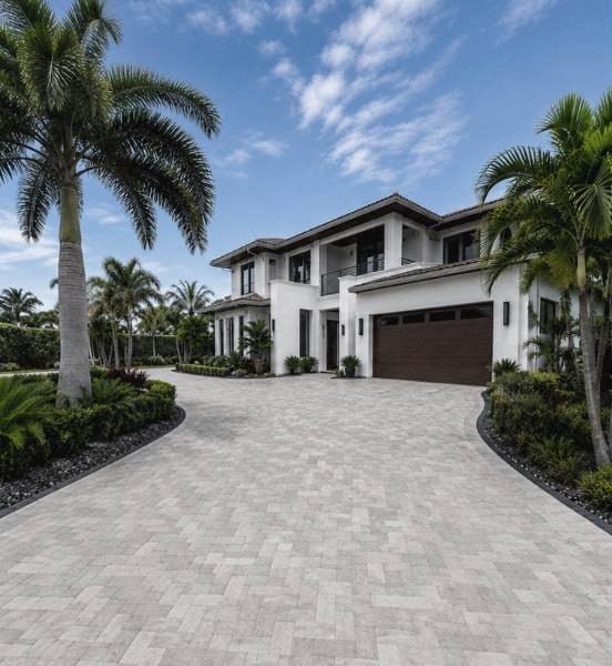 Paver driveway leading to a modern white Palm Beach estate framed by royal palms