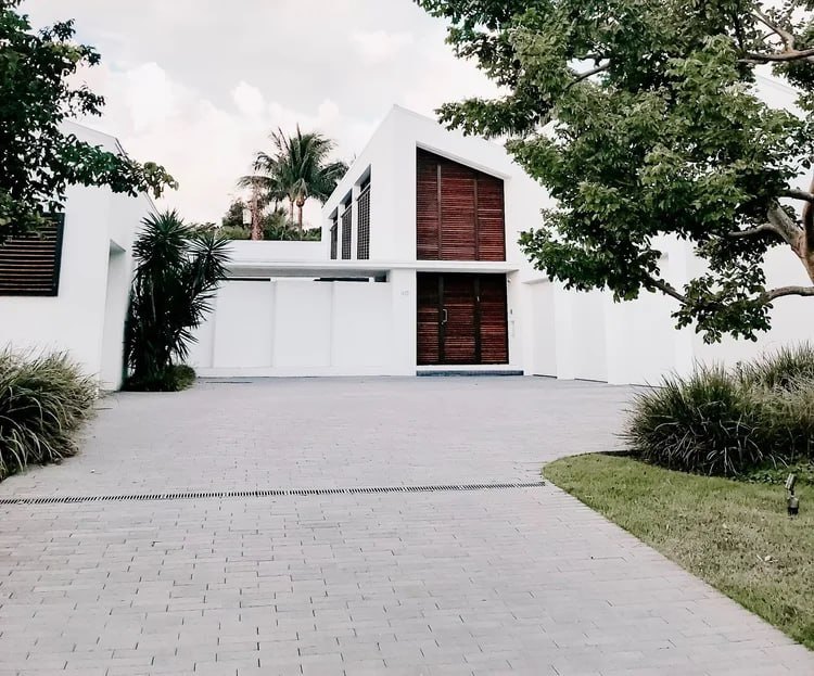Neatly laid paver driveway leading to a modern white Palm Beach home